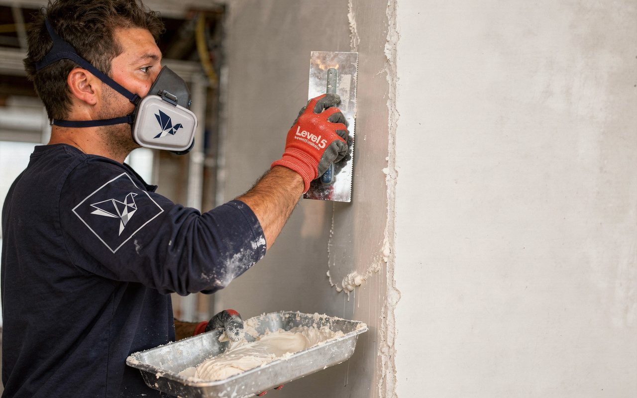 Blue Pigeon finisher applying joint compound to a drywall partition
