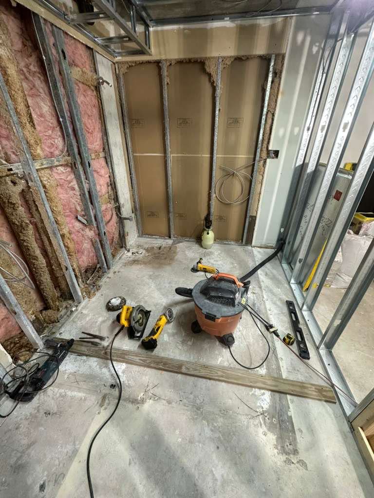 Empty room with steel stud framing and drywall backer installed, blueprints and tools staged neatly on the floor.