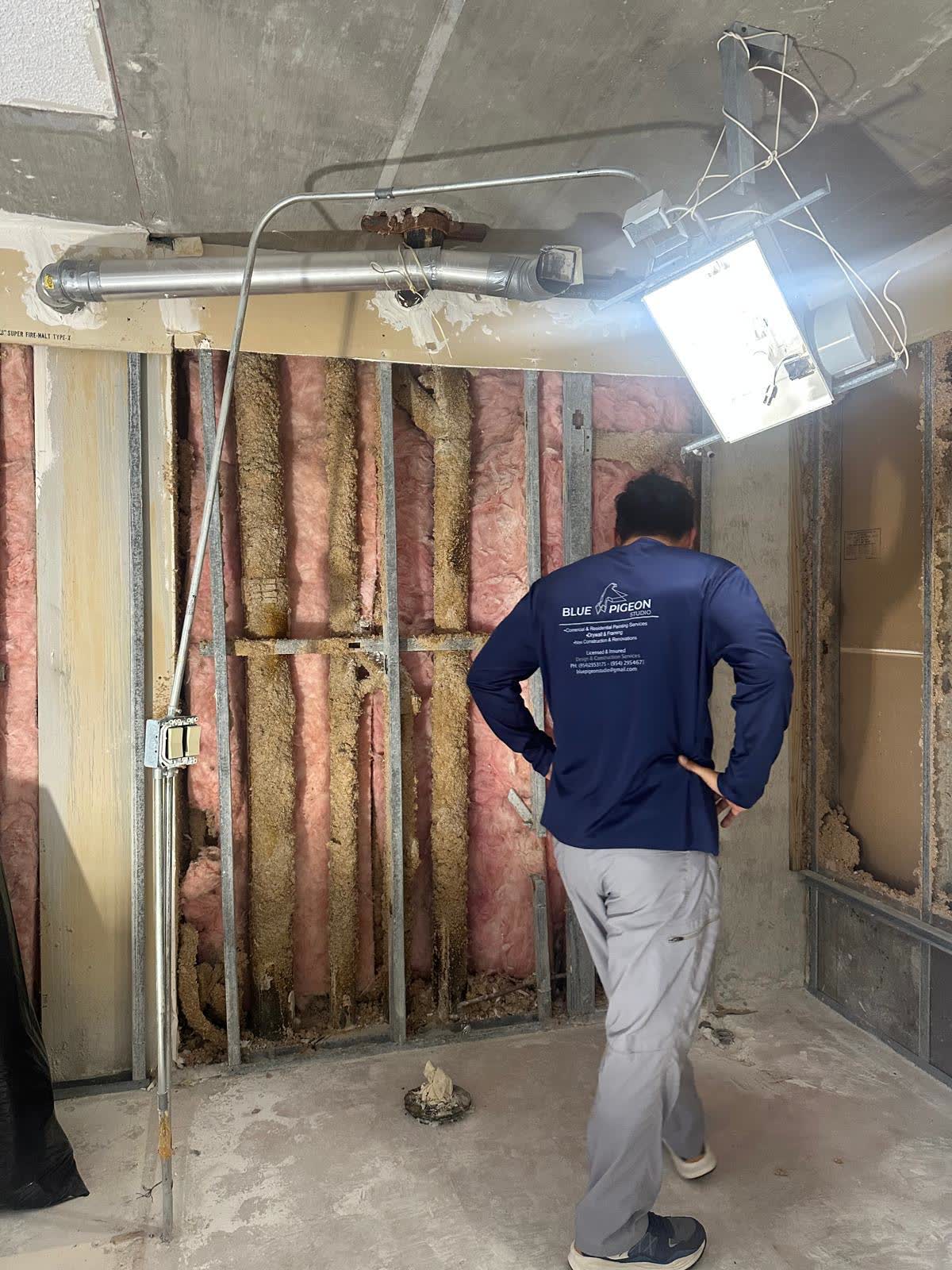 A crew member inspects exposed steel studs and insulation before drywall closes the wall.