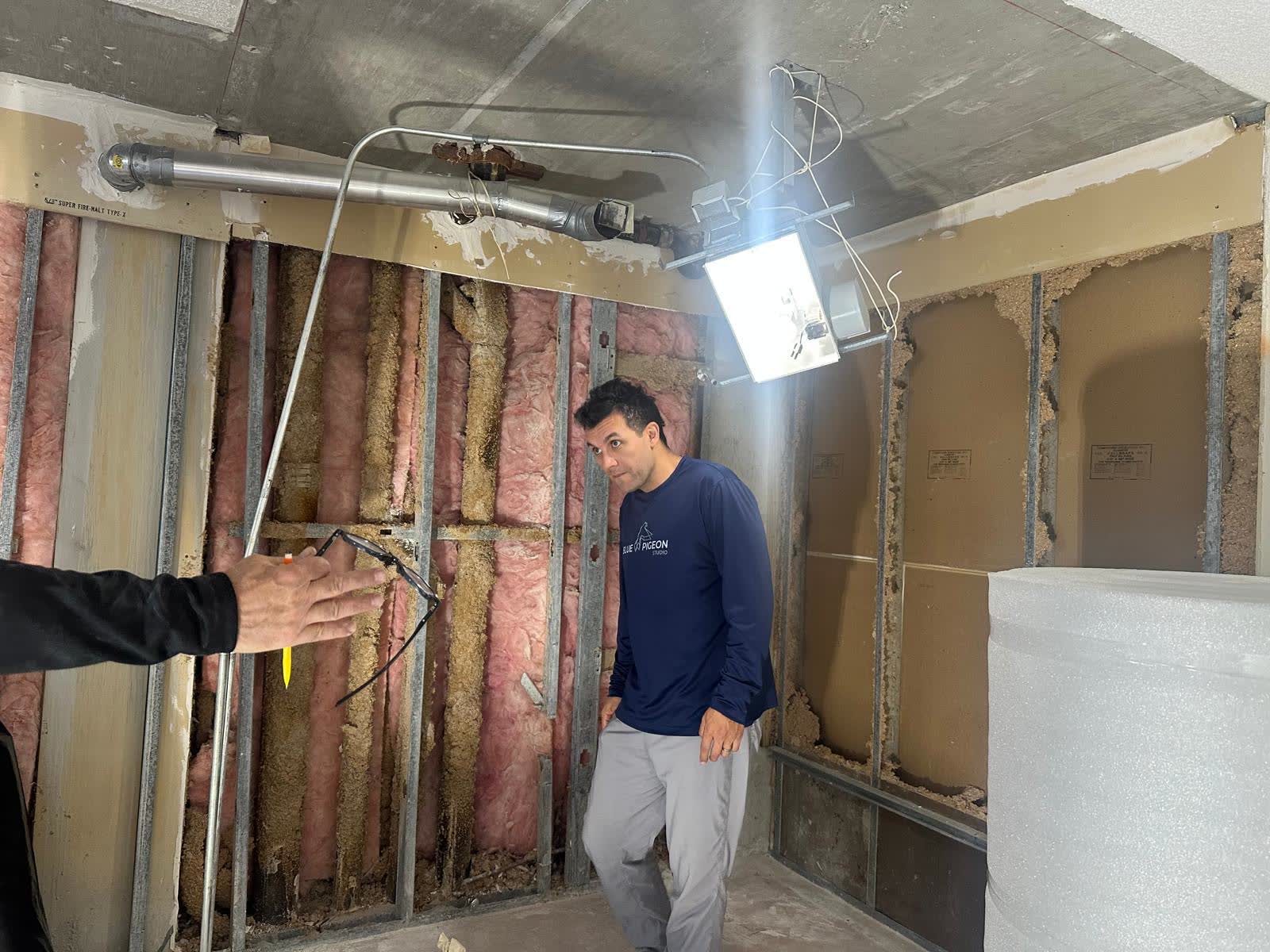 A room with drywall installed on one steel-stud wall, insulation exposed on the other, tools organized on the floor.