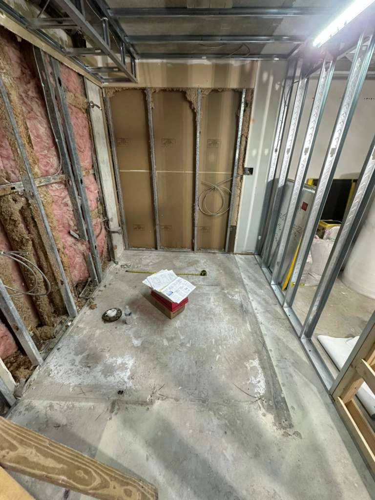 A worker in a respirator sprays texture finish across a wall inside a room stocked with wrapped materials.